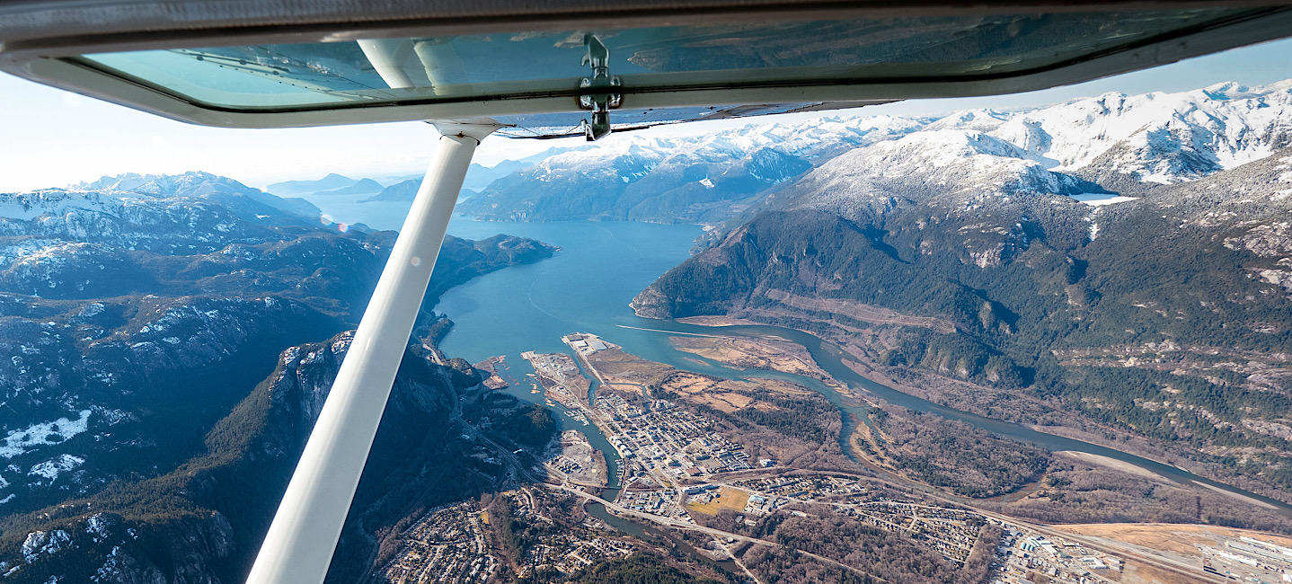 Endless view of Squamish, the turquoise Howe Sound and snowcapped coast mountains out of the open window of a scenic flight in Squamish, BC