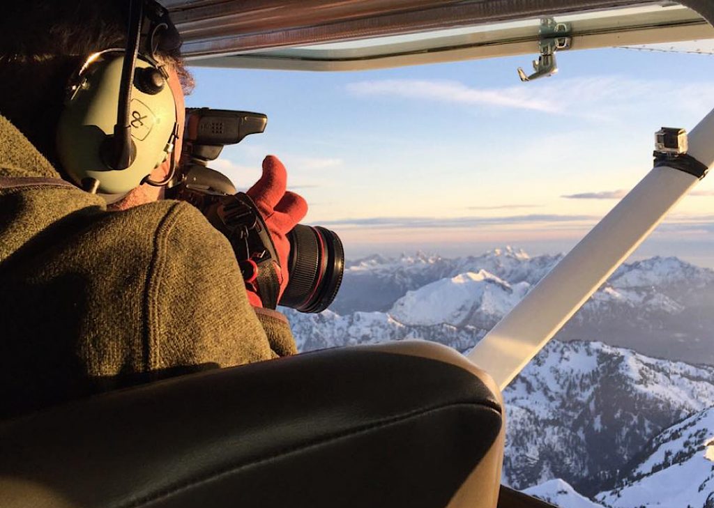 Dan Carr landscape photographer shooting mountains in winter through open window in Sea To Sky Air’s small plane