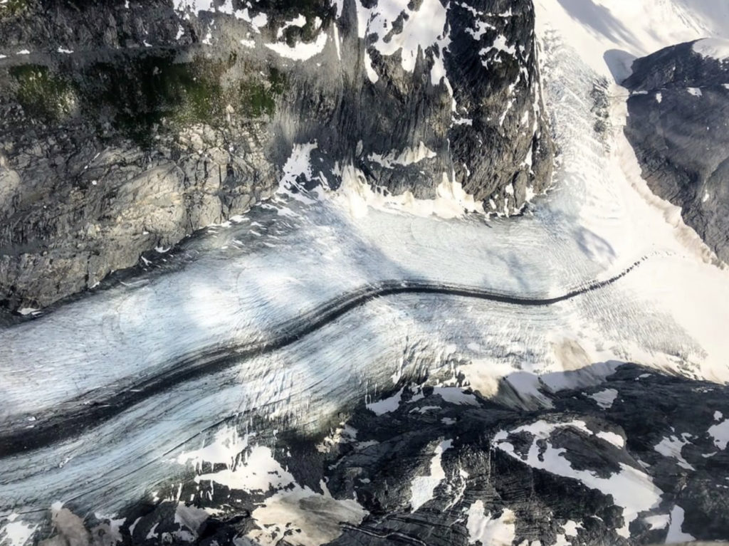 Birds-eye-view from a sightseeing flight of a glacier flowing through a valley with a big black moraine stripe down the middle in Clandenning Park near Squamish