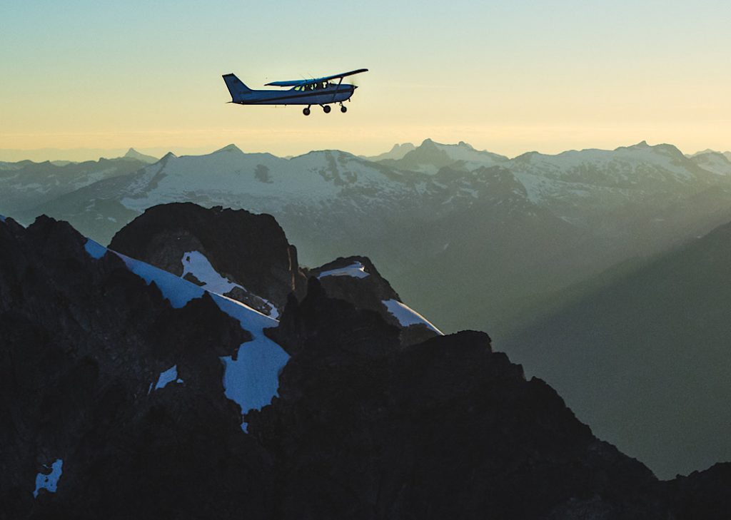 Sea To Sky Air plane flying over a silhouette of the Tantalus Range at sunset